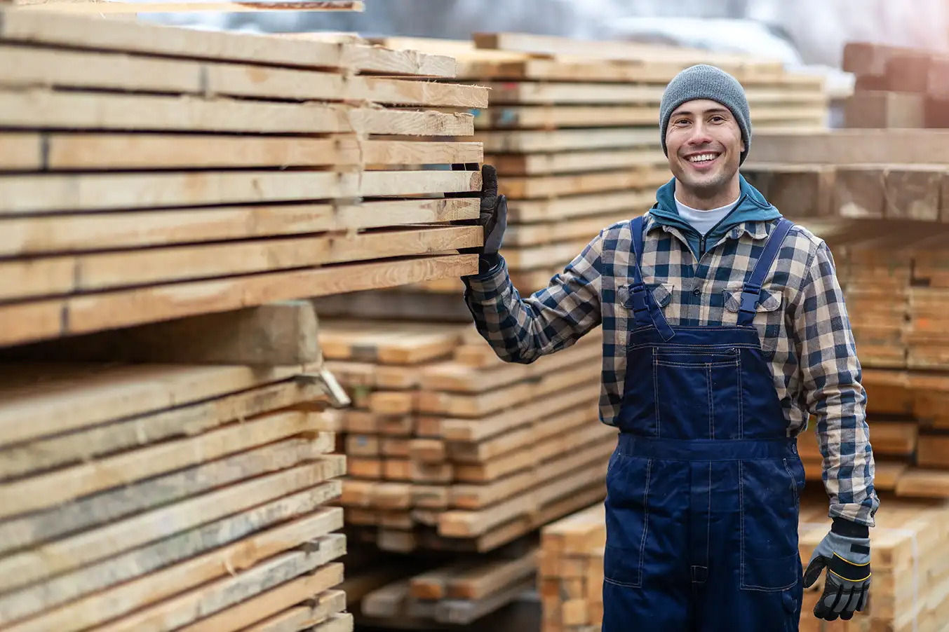 Smiling lumberyard worker next to stacks of construction boards